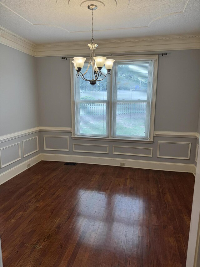 empty room featuring an inviting chandelier, ornamental molding, wainscoting, and dark wood-style floors