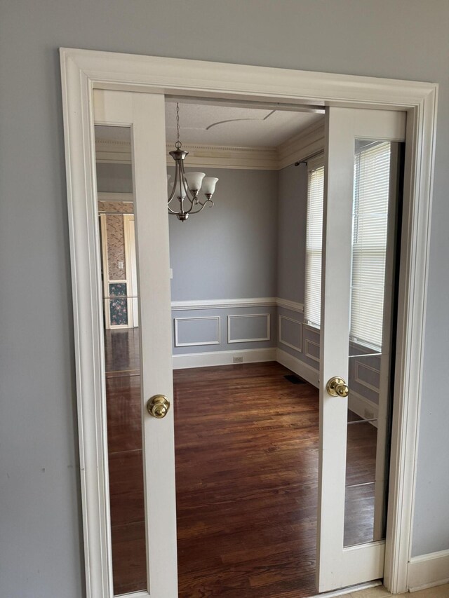 unfurnished dining area featuring crown molding, dark wood-style flooring, an inviting chandelier, and a wainscoted wall