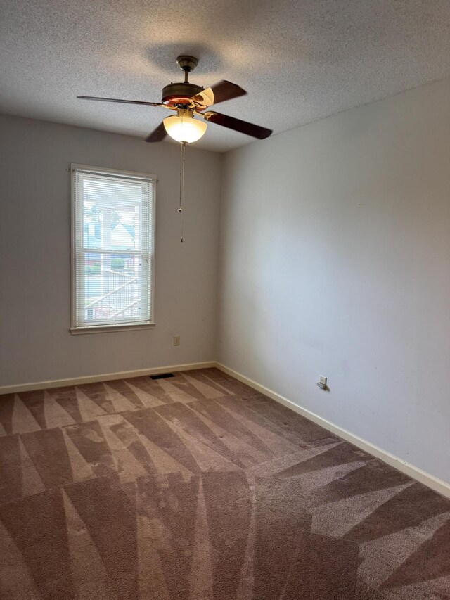 carpeted spare room with visible vents, a ceiling fan, a textured ceiling, and baseboards