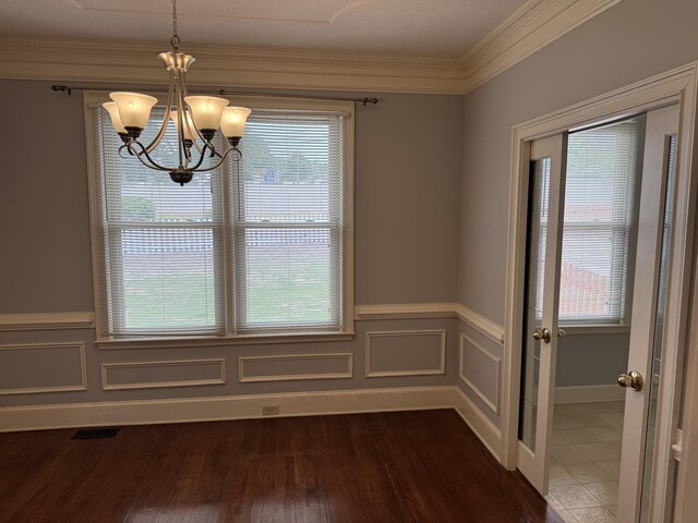 unfurnished dining area with a healthy amount of sunlight, a wainscoted wall, ornamental molding, and a notable chandelier