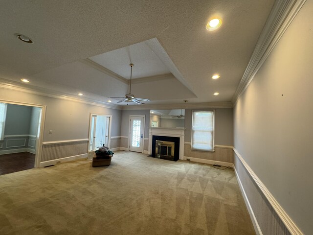 unfurnished living room with crown molding, carpet floors, ceiling fan, and wainscoting