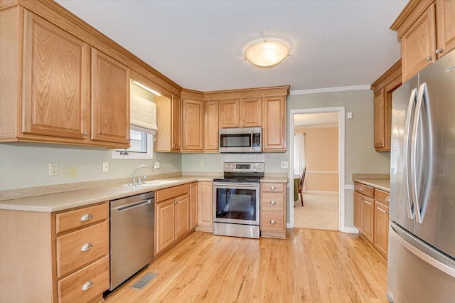 kitchen with light wood finished floors, stainless steel appliances, crown molding, light countertops, and a sink