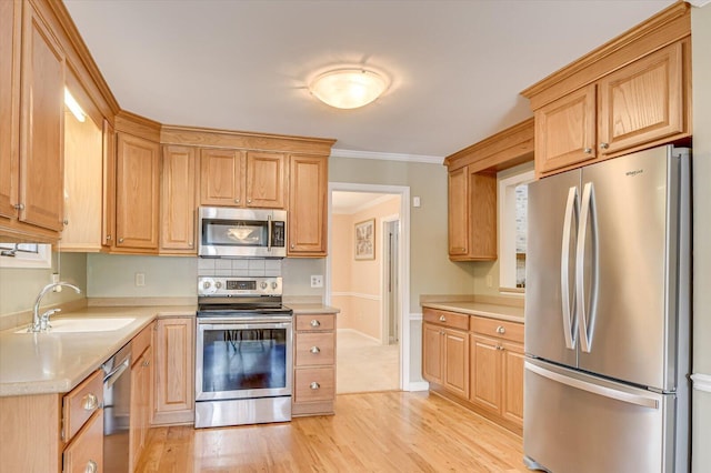 kitchen with crown molding, stainless steel appliances, light countertops, light wood-style floors, and a sink