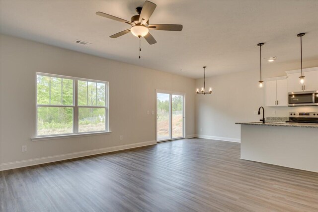 unfurnished living room with visible vents, baseboards, dark wood-style flooring, a sink, and ceiling fan with notable chandelier