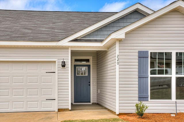 view of exterior entry with concrete driveway, roof with shingles, and an attached garage