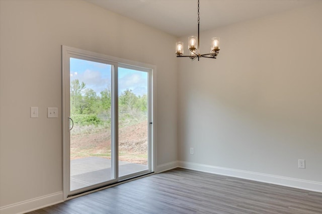 empty room with an inviting chandelier, wood finished floors, and baseboards