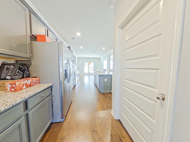 kitchen featuring light stone counters, stainless steel refrigerator with ice dispenser, crown molding, light hardwood / wood-style floors, and gray cabinets