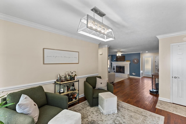 living room featuring a tiled fireplace, wood finished floors, crown molding, baseboards, and ceiling fan