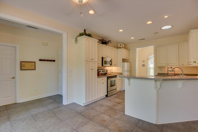 kitchen featuring white cabinets, light stone countertops, appliances with stainless steel finishes, kitchen peninsula, and a breakfast bar area