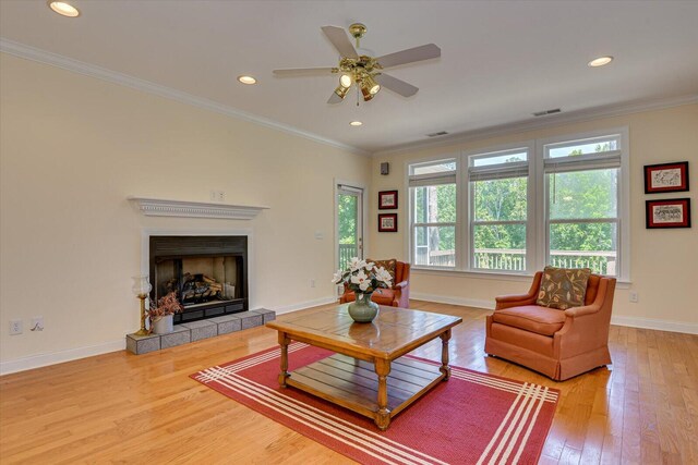 living room with a fireplace, ceiling fan, wood-type flooring, and crown molding