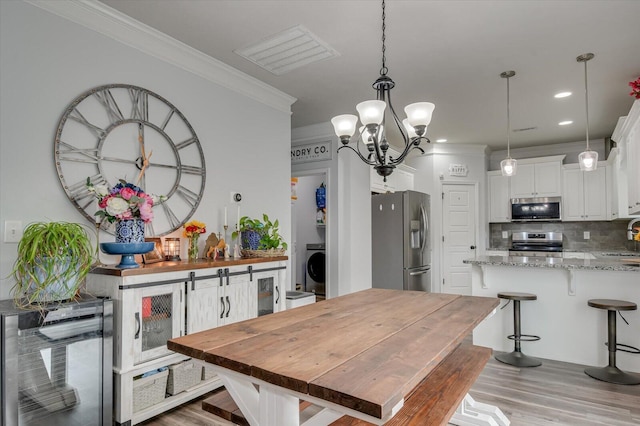 kitchen with white cabinetry, stainless steel appliances, tasteful backsplash, light stone counters, and crown molding