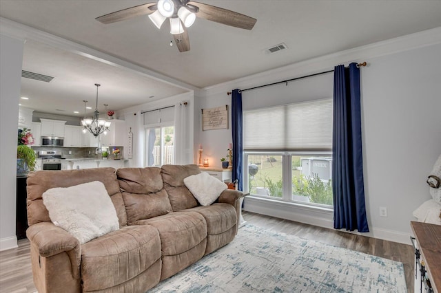 living room featuring a wealth of natural light, crown molding, ceiling fan with notable chandelier, and light wood-type flooring