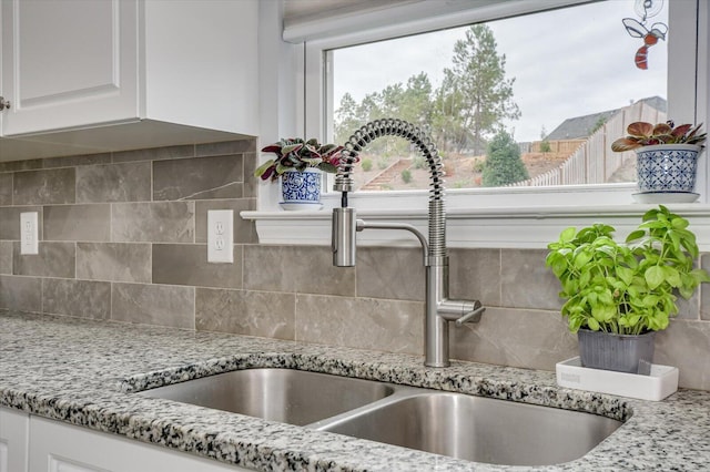 details featuring tasteful backsplash, light stone counters, sink, and white cabinets