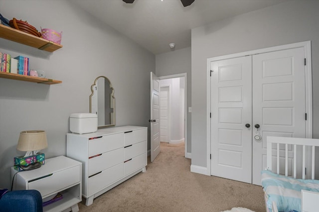 bedroom with ceiling fan, light colored carpet, a crib, and a closet