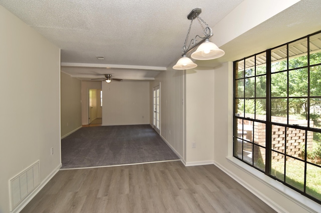 empty room featuring beam ceiling, ceiling fan, wood-type flooring, and a textured ceiling