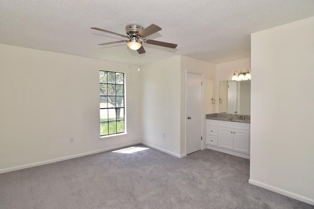 unfurnished bedroom featuring ceiling fan, sink, ensuite bathroom, light colored carpet, and a textured ceiling