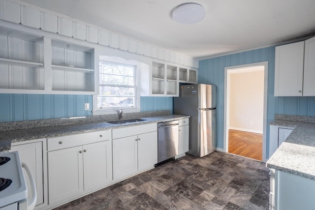 kitchen with white cabinetry, wood walls, stainless steel appliances, light stone counters, and sink