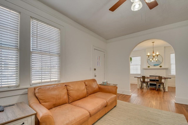 living room with arched walkways, crown molding, light wood-style floors, baseboards, and ceiling fan with notable chandelier