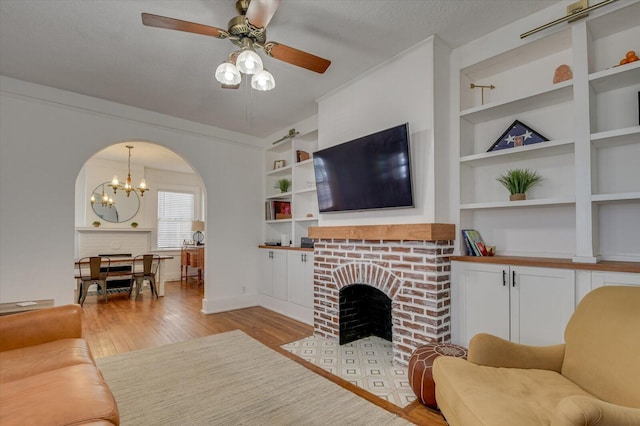 living room featuring light wood-style floors, a fireplace, built in shelves, and a textured ceiling