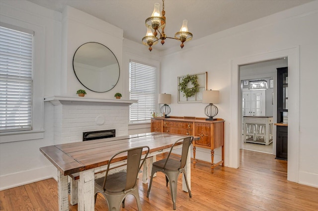 dining room with light wood finished floors, a notable chandelier, a fireplace, and a wealth of natural light