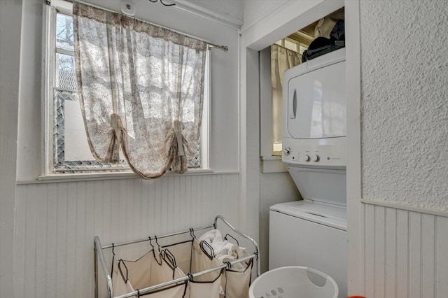 clothes washing area with a wealth of natural light, laundry area, stacked washer / dryer, and wainscoting