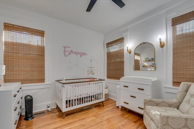 bedroom featuring ceiling fan, light wood-style flooring, visible vents, a crib, and crown molding