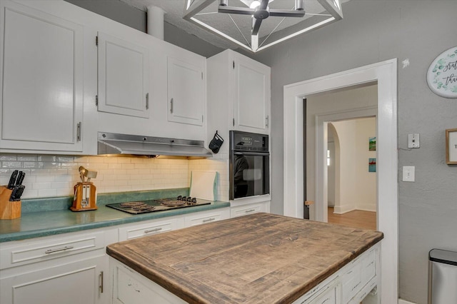 kitchen with arched walkways, decorative backsplash, under cabinet range hood, black appliances, and white cabinetry