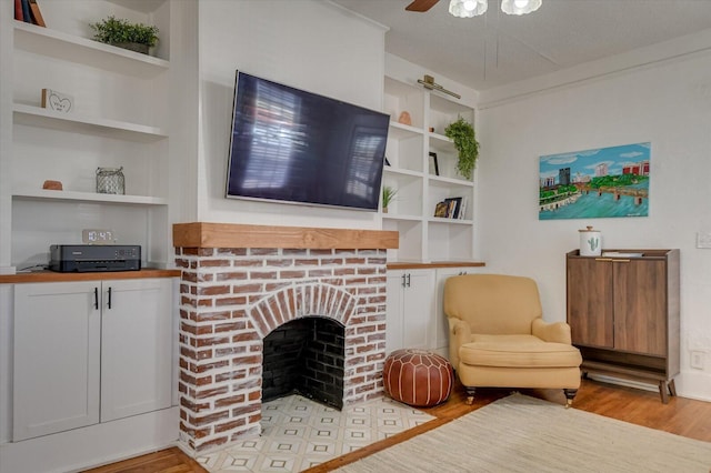 living area with light wood finished floors, built in features, ceiling fan, a textured ceiling, and a brick fireplace