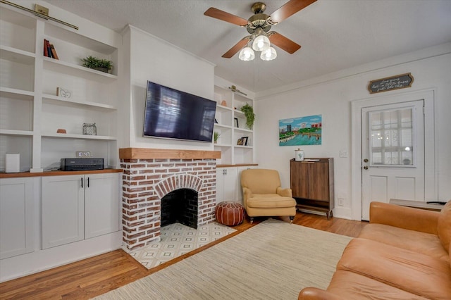 living room featuring a textured ceiling, light wood finished floors, a fireplace, and built in shelves