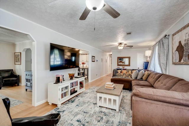 living area with arched walkways, crown molding, a textured ceiling, and light wood-style floors