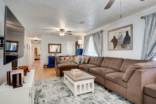 living room featuring visible vents, a ceiling fan, ornamental molding, wood finished floors, and a textured ceiling