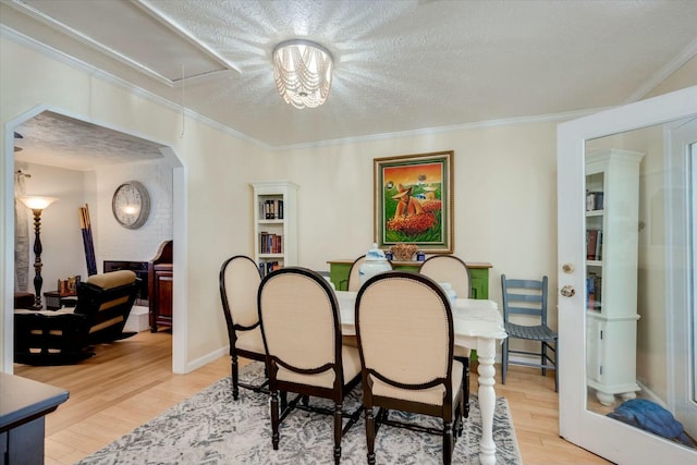 dining space with a textured ceiling, ornamental molding, wood finished floors, and attic access