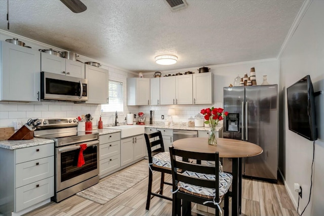 kitchen with light wood finished floors, visible vents, a sink, stainless steel appliances, and backsplash