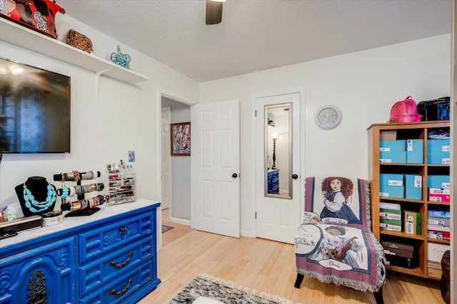 living area featuring light wood-style floors, ceiling fan, baseboards, and a textured ceiling