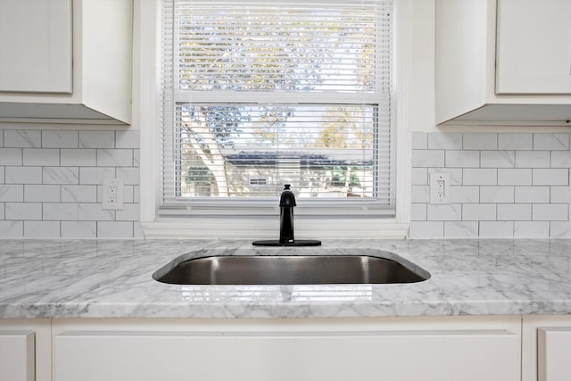 kitchen featuring light stone counters, white cabinets, sink, and backsplash