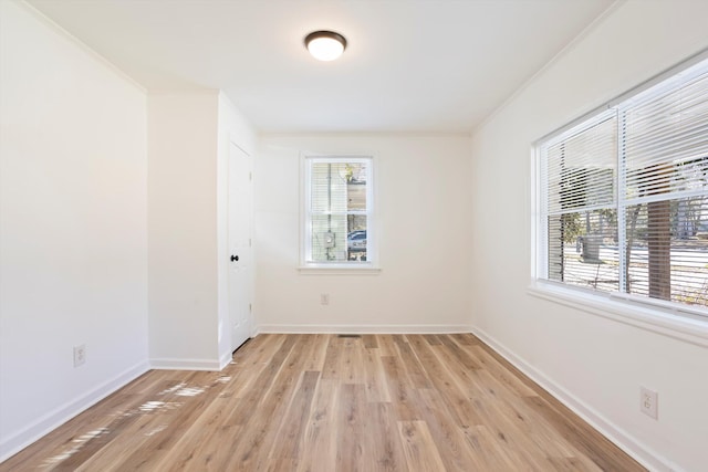 spare room featuring crown molding, a healthy amount of sunlight, and light hardwood / wood-style flooring