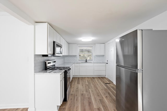 kitchen with sink, appliances with stainless steel finishes, white cabinets, decorative backsplash, and light wood-type flooring