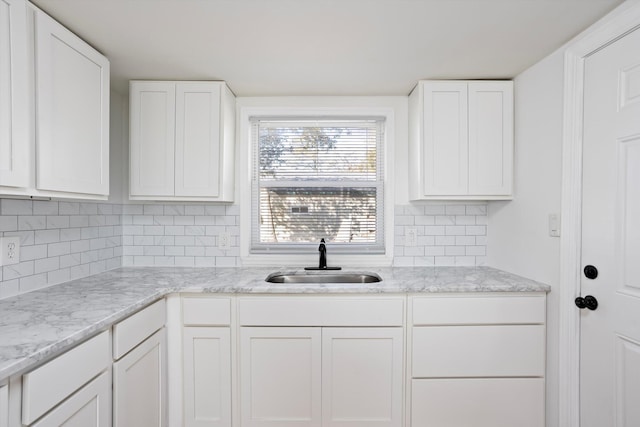 kitchen with white cabinetry, sink, backsplash, and light stone countertops