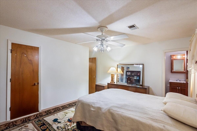 bedroom featuring ceiling fan, ensuite bathroom, and a textured ceiling