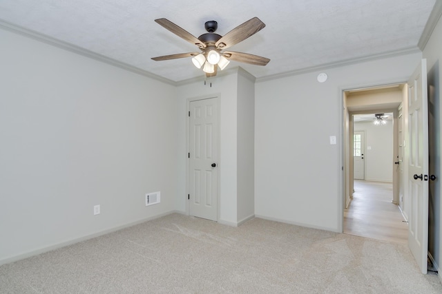 unfurnished bedroom with ceiling fan, light colored carpet, visible vents, baseboards, and ornamental molding