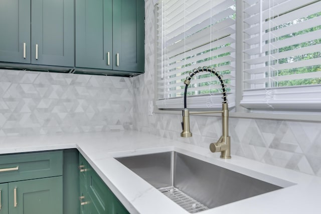 room details with a sink, light stone counters, green cabinets, and backsplash