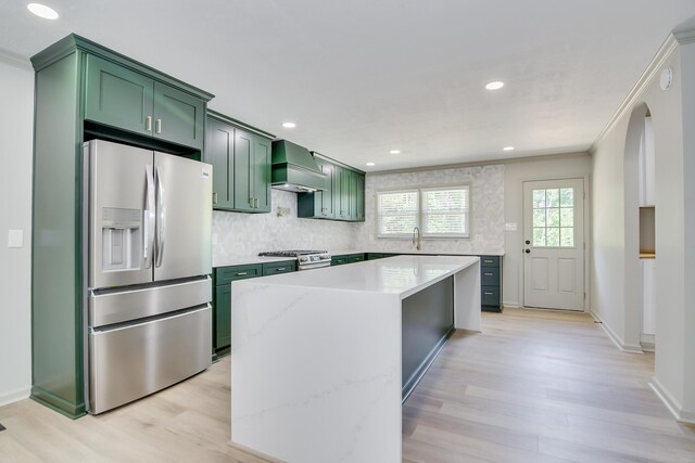 kitchen featuring a center island, light wood-type flooring, premium range hood, green cabinets, and stainless steel appliances