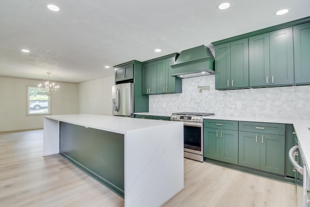 kitchen with an inviting chandelier, custom exhaust hood, light wood finished floors, appliances with stainless steel finishes, and green cabinets