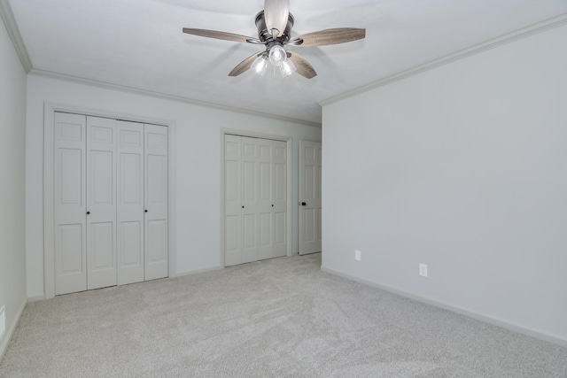 unfurnished bedroom featuring carpet floors, ornamental molding, baseboards, and two closets