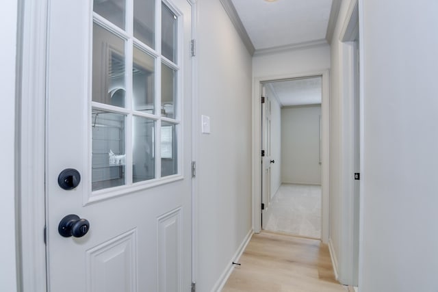 hall featuring crown molding, baseboards, and light wood-type flooring