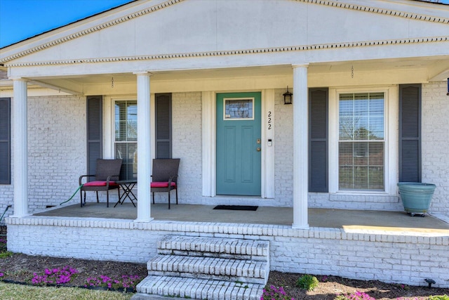 entrance to property with a porch and brick siding