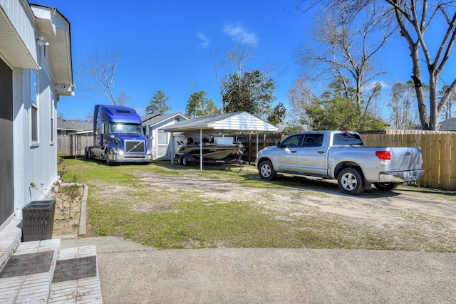 view of yard with cooling unit, fence, driveway, and a detached carport