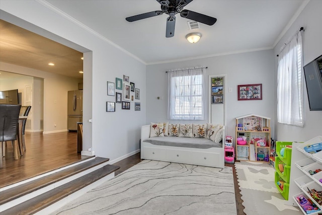 rec room with ceiling fan, wood finished floors, visible vents, baseboards, and ornamental molding