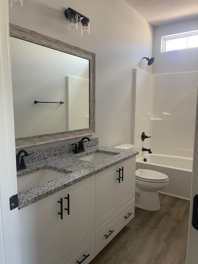 full bathroom with hardwood / wood-style floors, a textured ceiling, toilet, shower / washtub combination, and vanity