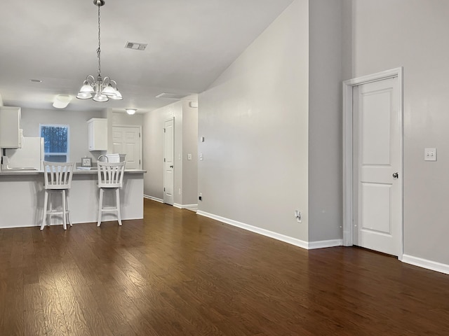 unfurnished living room featuring dark wood-style flooring, a notable chandelier, baseboards, and visible vents